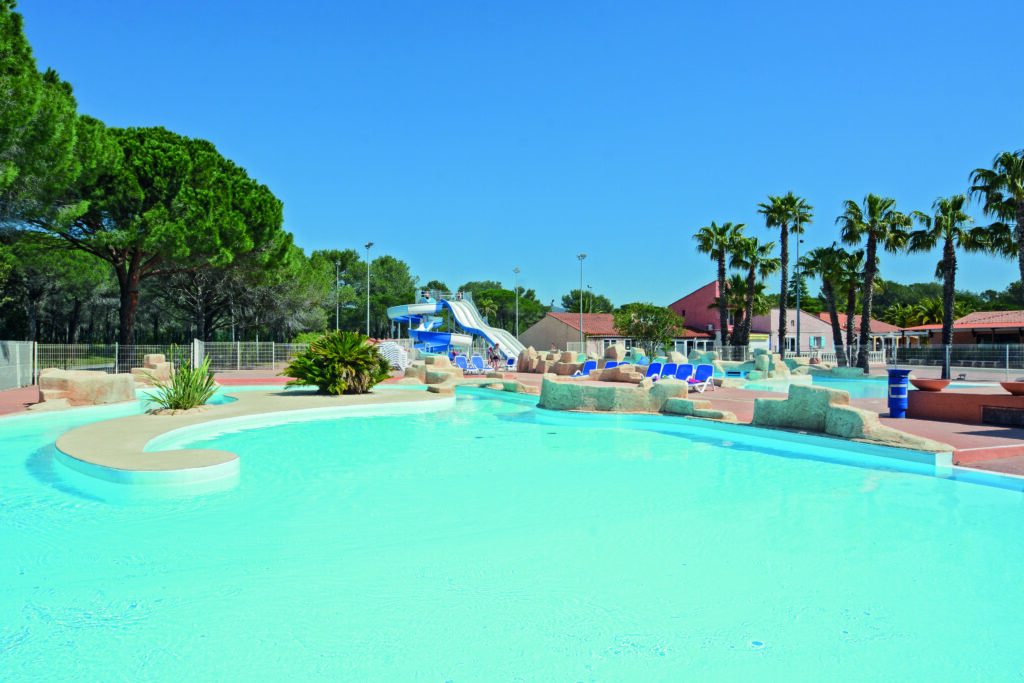 Overzicht van het waterpark Oasis Village: lagune met rotsen, palmbomen en waterglijbanen op de achtergrond